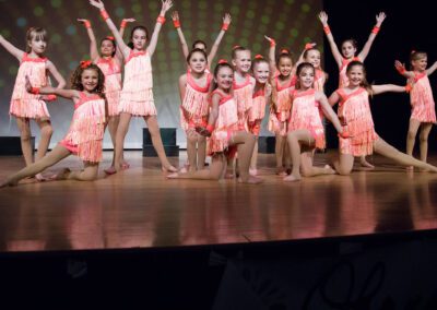 A group of young girls in orange dresses performing on stage.